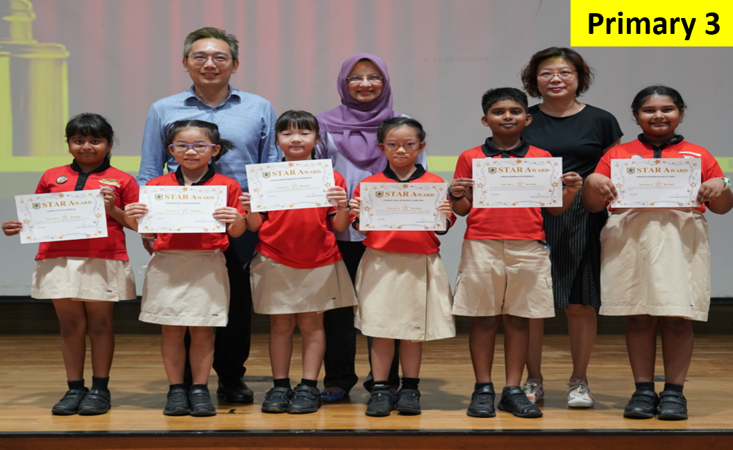 Six Primary 3 students hold Star Award certificates while posing with two teachers on a stage.